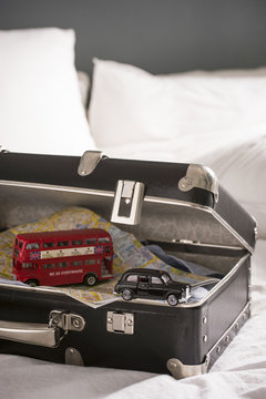 Open suitcase on bed with toy London bus and black cab