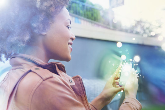 Young woman looking at smartphone with glowing lights coming out