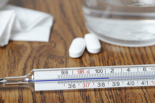 Galinstan thermometer showing elevated body temperature from fever, paracetamol pills, glass of water, tissue
