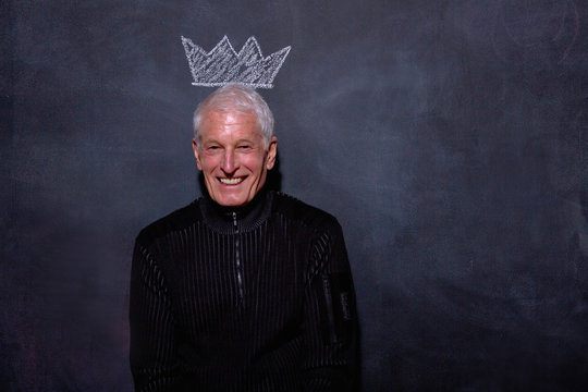 Portrait of senior man in front of chalked crown on blackboard