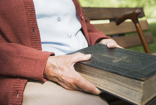 Mid section of senior woman, sitting on park bench, holding bible