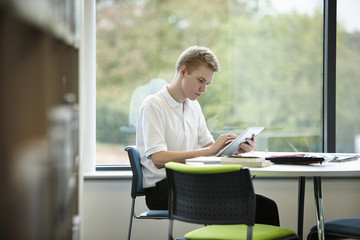 Teenage boy using digital tablet in library