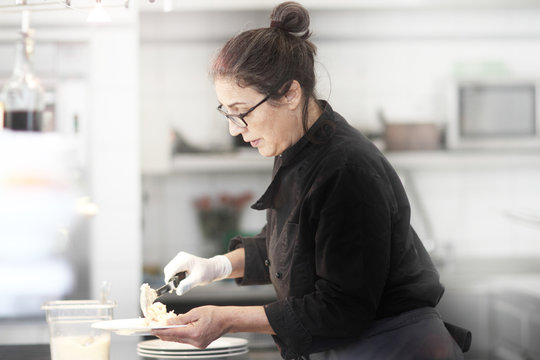 Woman working in restaurant kitchen, serving meal