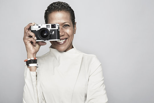 Studio portrait of happy mature woman holding up camera
