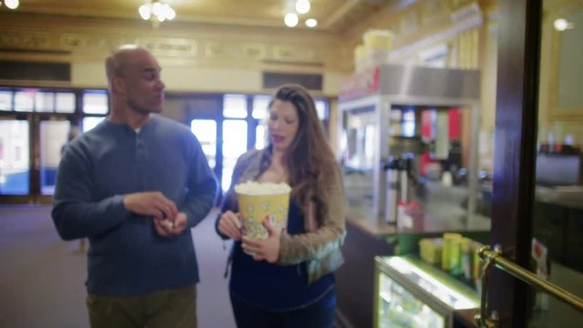 Couple walks through theater lobby, eating popcorn.  Medium shot, originally recorded in slow-motion, 4K at 60fps.