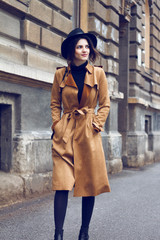 Young beautiful brunette enjoying and dancing in old city. She is wearing brown coat because is cold. On head she has nice stylish black hat. As an addition she has black handbag.