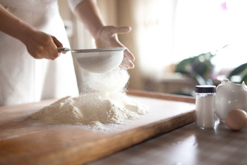 young woman sifting flour into bowl at the kitchen - 106954014