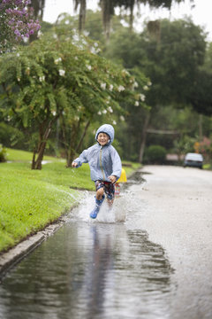 Boy in rubber boots running and splashing in rain puddle