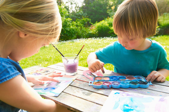 Brother and sister finger painting in garden
