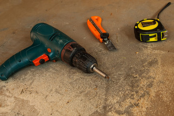 Drill and folding ruler, stationery knife on wooden background