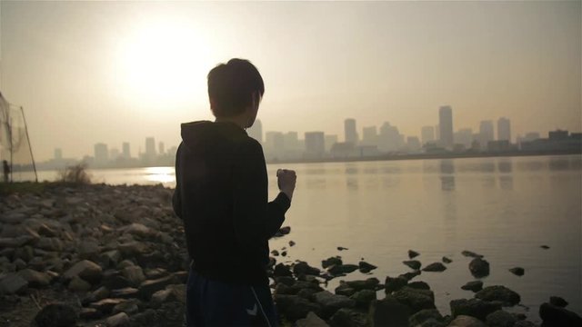 Young Japanese man shadow boxing at dawn down at the river in Japan