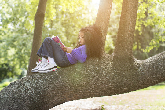 Young girl lying on tree branch reading book