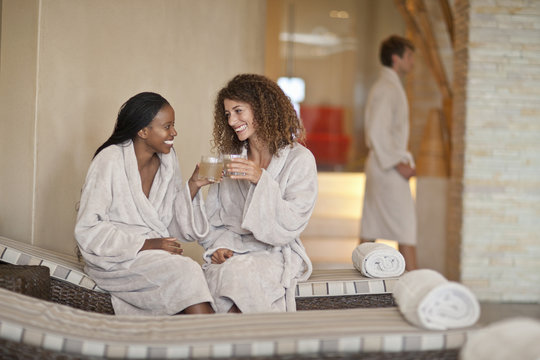 Women talking while sitting on lounge chair in spa