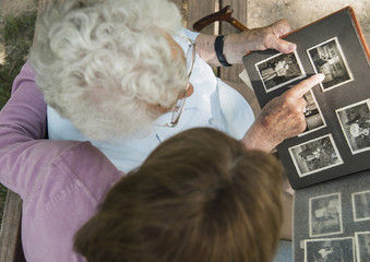 Senior woman sitting on park bench with granddaughter, looking at old photograph album