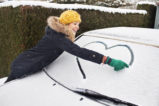 Woman drawing heart shape on snow covered windscreen