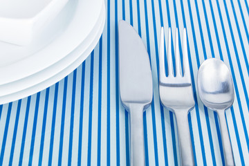 Geschirr, Messer, Gabel und Teelöffel auf glänzender, spiegelnder, blau gestreifter...