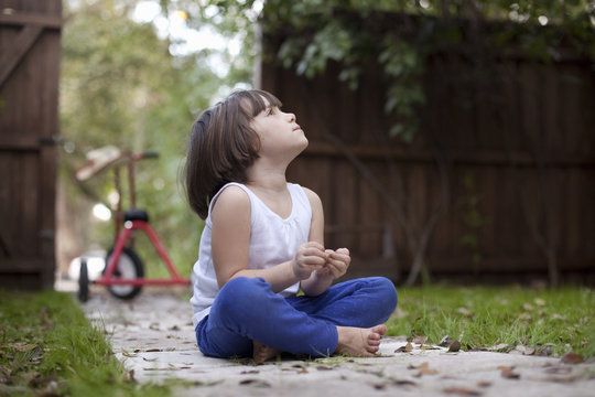 Four year old girl sitting on garden path gazing upward