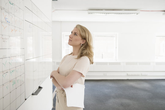 Young businesswoman contemplating whiteboard in empty office