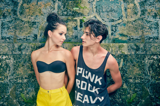 Young couple standing against wall, looking at each other