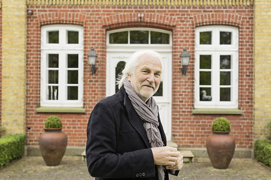 Portrait of senior man wearing jacket and scarf outside house
