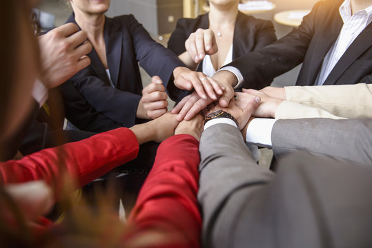 Over shoulder view of group of businesswomen and men with hands together in a circle
