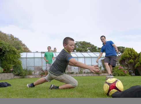 Father and sons playing football in garden