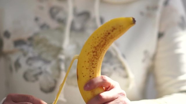 Banana Appears In Woman Hand. Woman Cleans Banana.