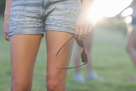 Cropped image of young woman in shorts holding sunglasses