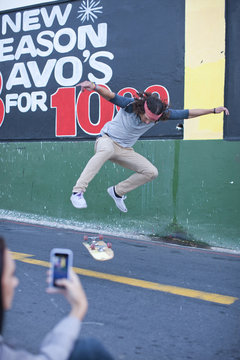 Young adult male being photographed on smartphone doing skateboarding trick