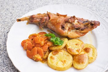 Gourmet roasted rabbit leg with glazed sweet carrot and baked potatoes choped on thin slices. Meal is served on the white simply plate and granit table isolated. Healty and light meal perfect for diet