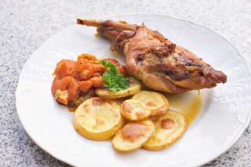Gourmet roasted rabbit leg with glazed sweet carrot and baked potatoes choped on thin slices. Meal is served on the white simply plate and granit table isolated. Healty and light meal perfect for diet