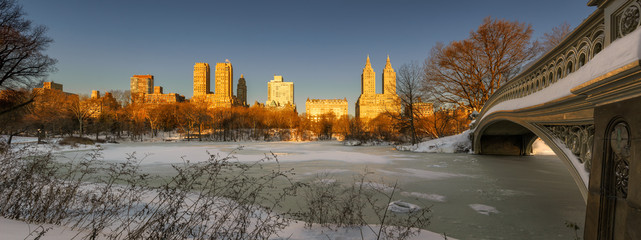 Panoramic winter sunrise on frozen Central Park Lake with Bow Bridge and view of Upper West Side buildings. Manhattan, New York City - obrazy, fototapety, plakaty