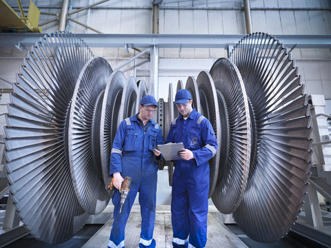 Engineers discussing notes in front of steam turbine in workshop