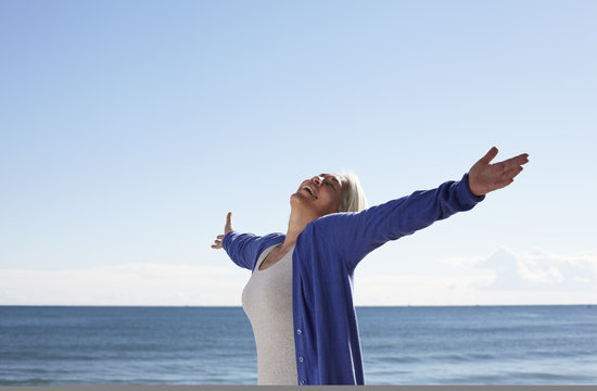 Mature woman on beach with arms outspread