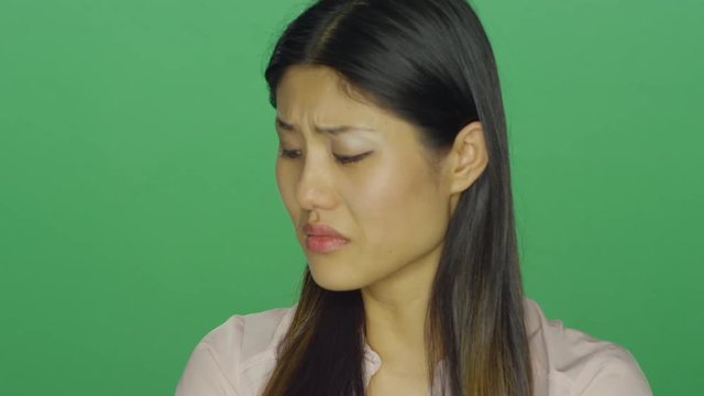 Beautiful Asian woman looking depressed, on a green screen studio background 