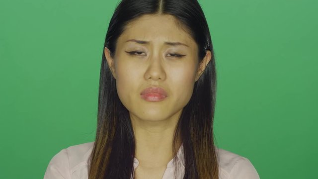 Beautiful Asian woman looking sad, on a green screen studio background