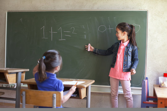 Girl by blackboard and sister at desk