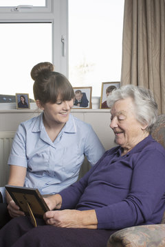 Personal care assistant looking at photograph with senior woman