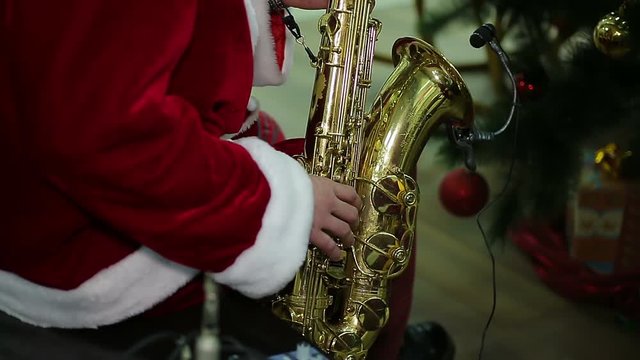 Man wearing Santa suit playing Xmas carol song on saxophone at festive concert