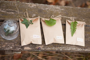 Three brown craft gift boxes decorated with fern and ivy leaves with glass box on wooden background