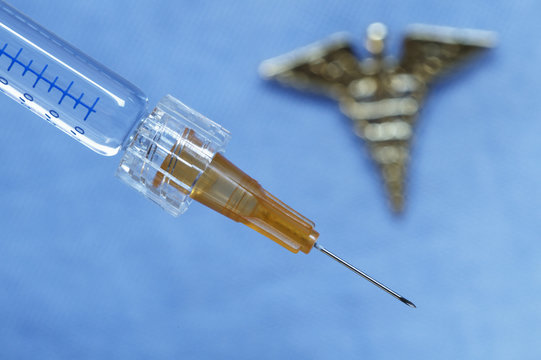 Close up of syringe with an out-of-focus caduceus in the background