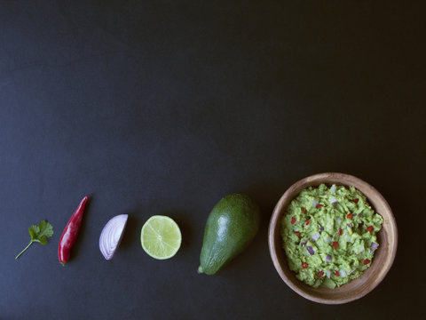 Wooden Bowl Of Guacamole And Its Ingredients On Black Background From Above 