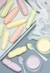 Homemade eclairs with pastel color icing on a baking sheet