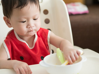 Asian toddler eat meal herself.