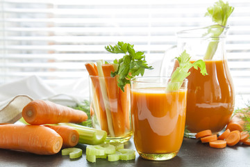 Fresh carrot juice with carrots, celery, dill and parsley on black background