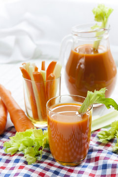 Fresh carrot juice with carrots and celery on checkered napkin light background