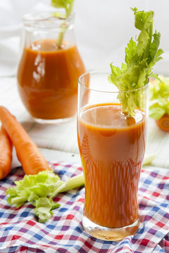 Fresh carrot juice with carrots and celery on checkered napkin light background