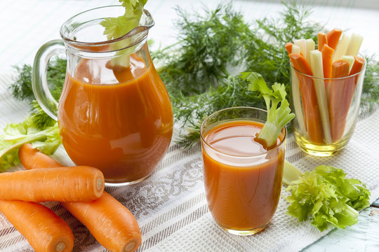 Fresh carrot juice with carrots, celery, dill and parsley on light background