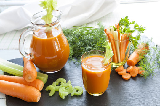 Fresh carrot juice with carrots, celery, dill and parsley on black background