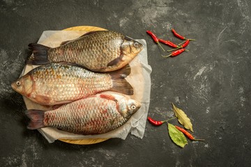 three fresh carps on a wooden board against old grey background